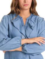 Blusa de lyocell con cuello a la base, escote en V y detalle de volados frontales. Presenta cierre con botones y mangas largas con puños elásticos fruncidos.