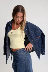 Camisa de jean azul oscuro, de corte oversize, con mangas largas y puños abotonados. Presenta bordados rojos en el pecho y un parche denim con el logo "BG" en la espalda.