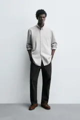 Camisa de corte regular fit confeccionada en tejido de algodón con estampado de cuadros pequeños. Presenta cuello abotonado, manga larga con puños abotonados, bolsillo plastrón en el pecho y cierre frontal con botones.