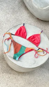 Bikini reversible de diseño triangular con tiras para atar y apliques de argollas metálicas. El conjunto presenta un estampado abstracto multicolor.