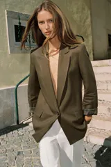 Blazer de lino color verde militar, con cuello solapa, hombreras y manga larga con puño revuelto con detalle a rayas. Cuenta con cierre frontal de un botón y bolsillos delanteros con solapa.