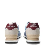 Championes New Balance modelo 574, color azul claro con gamuza azul más oscura, detalles en beige claro, rojo oscuro en el talón y logo 'N' en rojo oscuro con borde blanco.