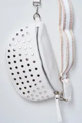 Riñonera blanca de cuero sintético con tachas metálicas plateadas en la parte frontal. Cuenta con cierre superior y una correa ajustable de diseño tejido en tonos blanco y tostado.