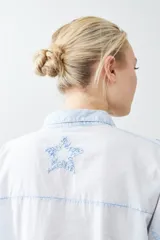 Camisa de corte recto y manga larga en color celeste claro, con diseño de estrellas bordadas en relieve en tono azul. Presenta cuello clásico y cierre frontal con botones.