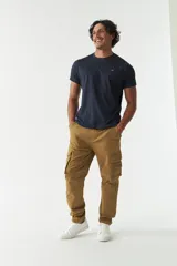 Pantalón cargo verde militar sin puños, de corte recto, con bolsillos laterales y traseros. Se ajusta a la cintura con cinturón de cuero marrón.