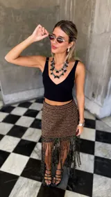 Falda tejida a mano en crochet, con diseño a rayas horizontales en tonos marrón y negro con hilos de lurex dorado. El ruedo presenta una cascada de flecos largos y finos en color negro.