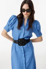 Cinturón de cuero vacuno con diseño de hebilla central circular y estructura de tiras entrelazadas. Cuenta con espalda elástica y cierre ajustable.