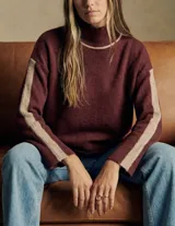 Polera de punto con calce oversize, cuello alto y mangas largas. Presenta un diseño en color negro con franjas laterales en las mangas y detalle en el cuello en tono bronce con acabado brillante.