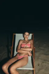 Braguita de bikini de tiro medio, con textura gofrada en tonos coral y naranja, y forro interior fucsia. Presenta un nudo decorativo en el lateral izquierdo.