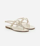 Sandalia plana color beige con tiras finas y tira central decorada con colgantes metálicos dorados en forma de conchas marinas. Cuenta con cierre de hebilla ajustable en el tobillo.