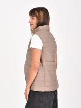 Chaleco acolchado de diseño matelasse, color beige, con cuello alto, cierre frontal y bolsillos laterales.