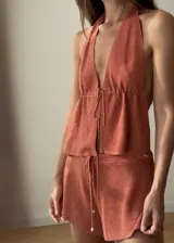 Top de tejido de punto con acabado brillante, diseño halter con escote profundo y espalda descubierta. Presenta un cierre frontal mediante cordones ajustables.