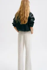 Jean de tiro regular y corte acampanado, confeccionado en denim de algodón color blanco. Presenta diseño de cinco bolsillos y detalles de costuras con ribetes bordados ondulados en el frente y los laterales.