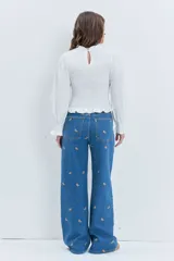 Jean de corte wide leg en color azul medio, con diseño de pequeños bordados dispersos en toda la prenda. Presenta cierre frontal con botón y bolsillos laterales.