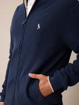 Cardigan de punto en color gris, con cierre frontal completo, cuello tipo mao y puños acanalados. Presenta un pequeño logo bordado en el pecho y detalles en contraste en el interior del cuello y puños.