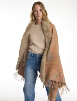 Ruana tejida con estampado de arabescos en tonos beige, con cuello y bordes frontales decorados con aplique de piel sintética y terminación con flecos en el ruedo.