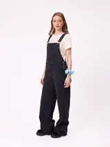 Mono de jean negro con diseño de jardinera, de corte recto y holgado, con bolsillos frontales y laterales.