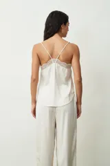 Blusa de tirantes finos en color negro, confeccionada en satén con sutiles brillos, destacando por un delicado detalle de encaje en el escote en V.