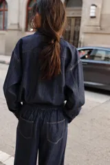 Jeans de tiro alto color azul oscuro, con cintura elástica en la espalda, bolsillos delanteros y bolsillos de plastrón en la espalda. Presenta pernera ancha y cierre frontal con cremallera y botón a presión.