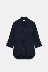 Camisa estilo safari de color azul marino con textura efecto arrugado, cuello solapa, mangas remangadas y cierre frontal con botones. Presenta bolsillos delanteros con solapa y un cinturón fino ajustable en la cintura.