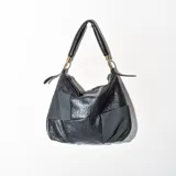 Cartera tipo hobo de cuero sintético negro con paneles de tela texturizada. Tiene doble asa de hombro y cierre superior con cremallera.