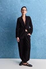 Pantalón negro de tiro alto y calce holgado, con pierna amplia, bolsillos laterales y puños ajustados con botones en los tobillos.