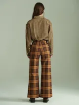 Pantalón de tiro alto con corte ancho y recto, confeccionado en tela de algodón con estampado de cuadros escoceses en tonos azul marino, verde y rojo. Presenta cierre frontal oculto con botones internos y pasacintos en la cintura.