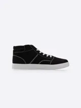 Bota de lona estilo urbano, color negro con costuras blancas visibles, cordones blancos y suela de goma blanca.