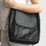 Cartera negra de cuero convertible en mochila, con tapa superior, cierre metálico, terminaciones trenzadas, forro de gabardina de algodón, bolsillos internos y externos con cierre.