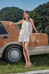 Cartera de gamuza color camel con diseño de flecos largos en la parte inferior y tachas metálicas circulares en el frente. Cuenta con correa larga ajustable de cuero y cierre superior.