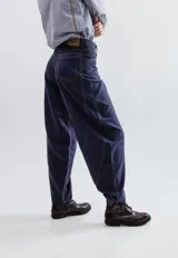 Pantalon de gabardina corte balloon, color azul oscuro, con costuras en contraste y diseño de paneles curvos. Presenta bolsillos traseros superpuestos y cierre frontal con botón metálico.