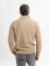Buzo de tejido de punto color beige con cuello alto y cierre frontal parcial. Presenta puños y ruedo acanalados.