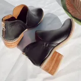 Botín de cuero vacuno color negro, con diseño de corte lateral, cierre metálico en el talón y taco foliado de madera en tono natural.