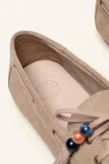 Mocasín estilo náutico de gamuza marrón, con cordones de cuero, borla decorativa y cuentas de colores en el empeine.