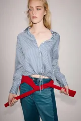 Camisa de cuello solapa y manga larga, con bajo ajustable mediante cordones y cierre frontal con botones ocultos. Diseño a rayas blancas y azules.