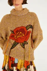 Sweater tejido color mostaza con cuello alto, mangas largas y un gran bordado floral en el frente con detalles colgantes.