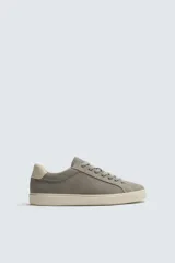 Zapatilla deportiva de hombre confeccionada en piel con acabado de serraje. Presenta un diseño minimalista con cordones al tono y un detalle en contraste de color en la pieza del talón. Cuenta con una suela de goma con volumen.