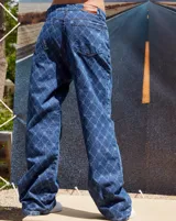 Jean de tiro bajo y corte oversize, confeccionado en denim azul con grabado láser de monograma en patrón de rombos. Presenta avíos metálicos y diseño de pierna ancha.