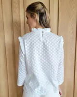Blusa blanca de manga larga con cuello alto y volados en cuello y hombros.