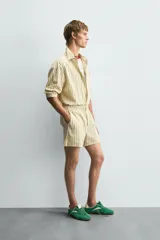 Shorts de hombre confeccionados en algodón con estampado de rayas verticales amarillas y blancas. Presenta cintura elástica, bolsillos frontales y un pequeño bordado de un pez en la parte inferior derecha.