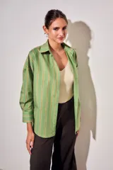 Camisa de corte oversize con estampado de rayas verticales en tonos verde, blanco y ocre. Presenta cuello clásico, cierre frontal con botones, bolsillo en el pecho y mangas largas con puños abotonados.