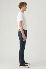 Pantalón de jean corte slim taper, de color azul oscuro con costuras en contraste. Presenta diseño de cinco bolsillos, cierre de botón y bragueta con cremallera.
