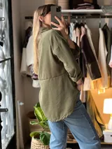 Camisa verde militar de corte oversize y largo asimétrico, con cuello clásico, mangas largas remangadas y cierre frontal con botones.