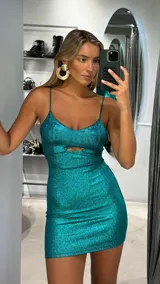 Vestido corto de fiesta color verde esmeralda con acabado brillante. Presenta breteles finos, escote redondo y una abertura frontal tipo cut-out bajo el busto. Su diseño es ajustado al cuerpo.