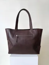 Cartera tipo shopper de cuero marrón texturado, con doble asa de hombro y un bolsillo frontal amplio con cierre de imán.