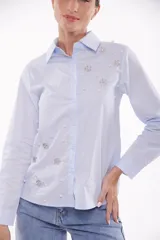Camisa celeste con cuello clásico, abotonada al frente y decorada con apliques de perlas y strass.