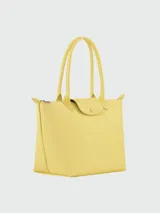 Bolso tote de tamaño mediano, confeccionado en cuero sintético de color amarillo. Presenta un diseño minimalista con cierre de cremallera superior, solapa frontal con botón a presión y doble asa de hombro.