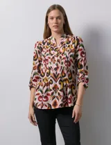 Blusa de gasa estampada con diseño geométrico multicolor, cuello a la base con escote en V y abertura frontal con botones. Presenta detalle de plisado en la parte delantera y mangas largas con sistema de ajuste mediante presilla y botón.