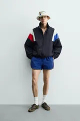 Chaqueta técnica de corte relajado con cuello subido y cierre frontal de cremallera bidireccional. Presenta un diseño color block en tonos azul marino, blanco, rojo y azul eléctrico. Incluye bolsillos frontales de vivo, puños y ruedo elásticos, y forro interior de red.