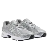 Championes New Balance modelo 740, con estética inspirada en el running de los años 2000. Presentan una parte superior de malla gris con superposiciones sintéticas metalizadas, entresuela blanca con tecnología de amortiguación y suela de goma negra.